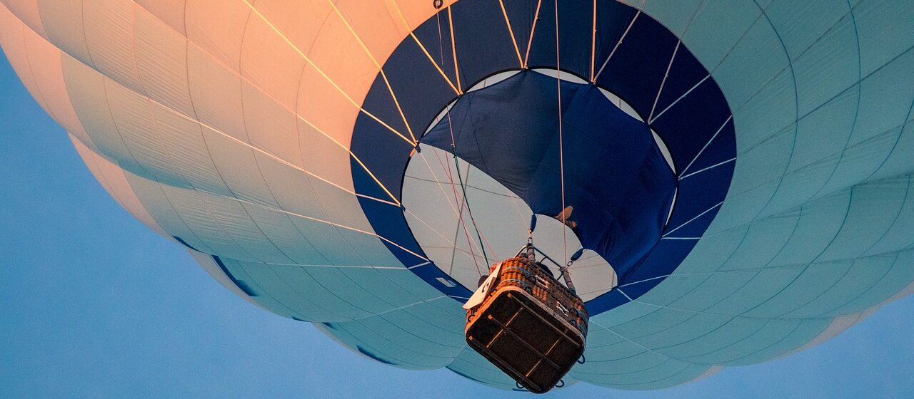 Une montgolfière s'élève doucement dans le ciel au lever du soleil, offrant une vue imprenable et paisible sur le paysage en dessous.
